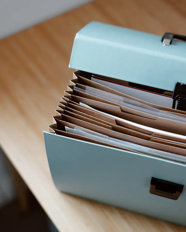 A pale blue accordion file on a wooden desk, its pockets full of sorted papers