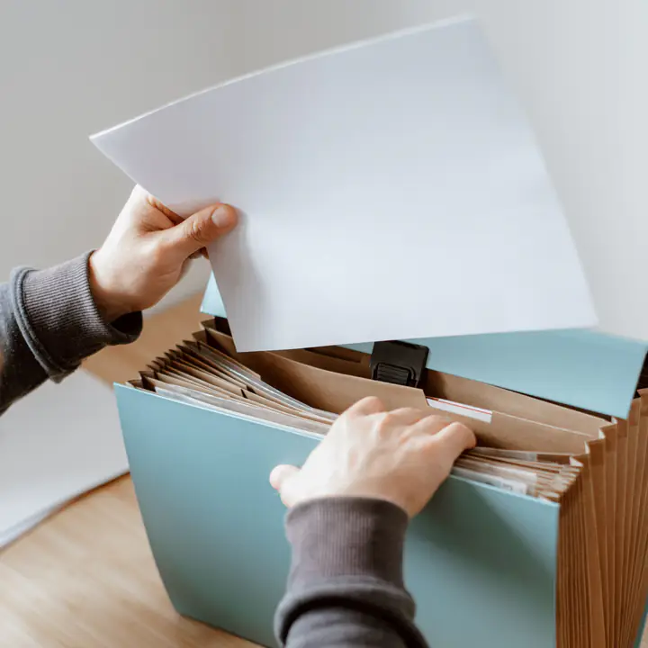 Hands filing a sheet of paper into a pale blue accordion file