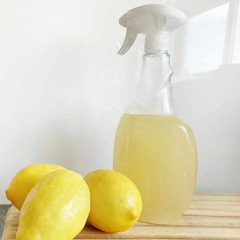 Three lemons on a wooden board beside a glass spray bottle of lemon cleaner