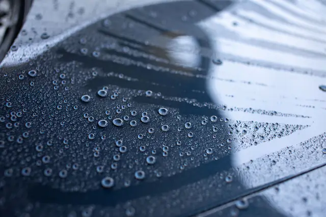 Round water beads sitting on a coated dark blue car panel