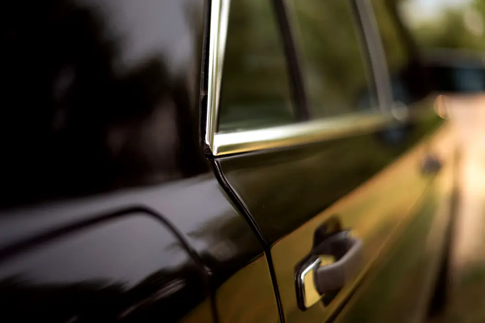 A glossy black vintage car door with a chrome handle, after polishing