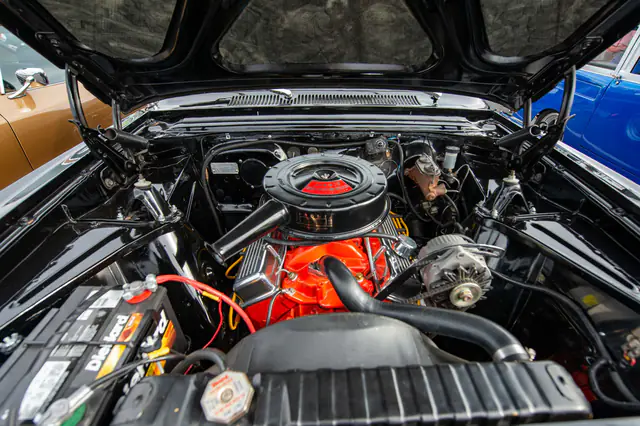 A clean classic V8 engine bay with an orange engine block and a chrome air cleaner