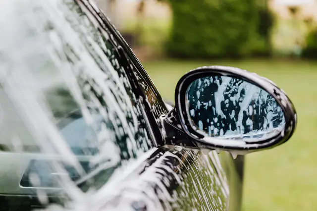 Thick white soap foam running down a black car door and side mirror