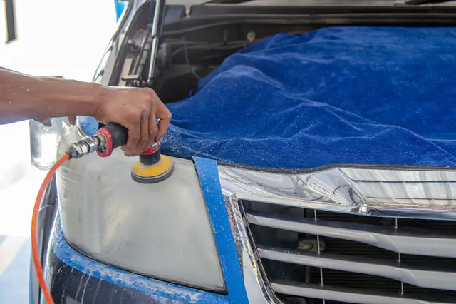 A small orbital sander restoring a cloudy headlight, with the paint around it taped off