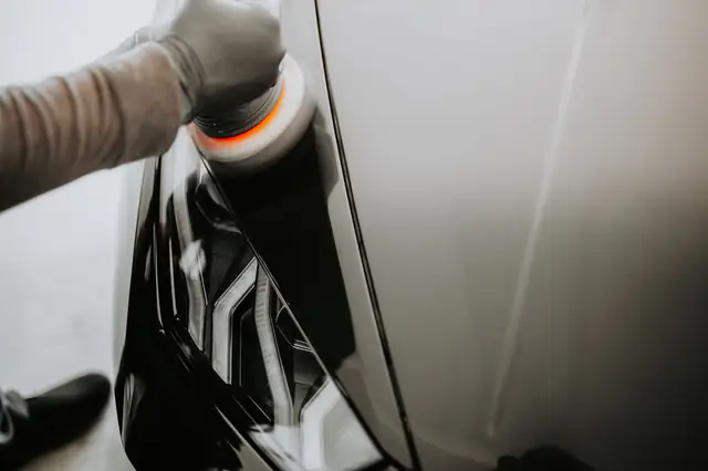 A dual action polisher with an orange pad working on glossy black paint