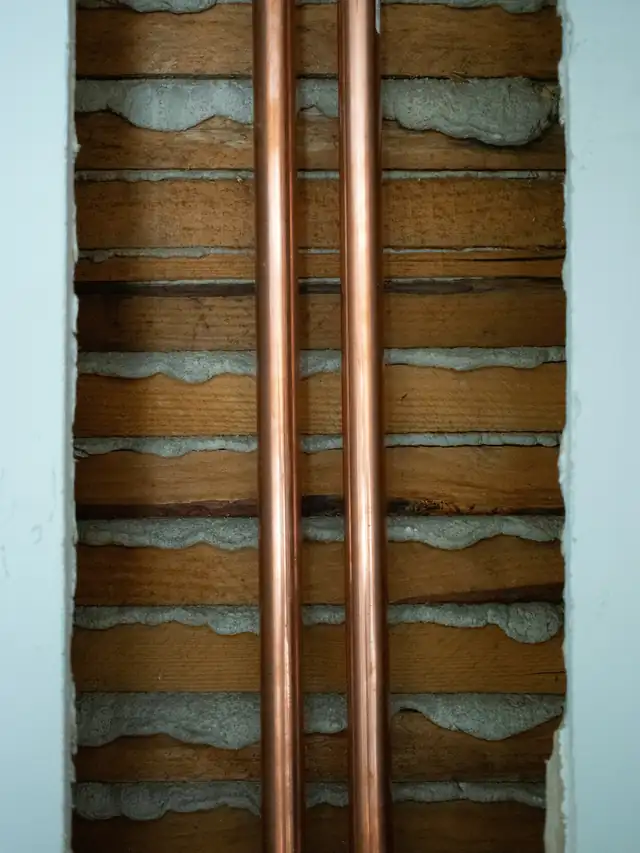 Two new copper water lines running up through an open plaster and lath wall