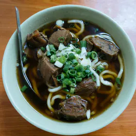 A bowl of beef noodle soup with braised beef and scallions, seen from above