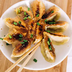 Pan-fried dumplings with crisp brown bottoms arranged in a star on a white plate