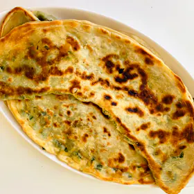 Golden scallion pancakes with charred spots on an oval plate