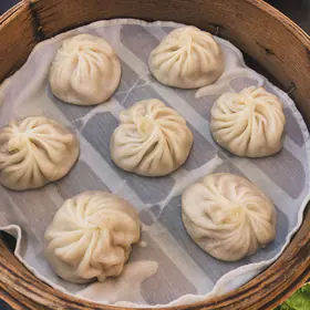 Eight soup dumplings on a cloth liner in a bamboo steamer, seen from above
