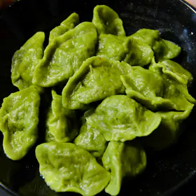 Bright green spinach dumplings piled in a black bowl
