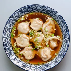 Wontons in a red-brown chili broth in a blue and white bowl